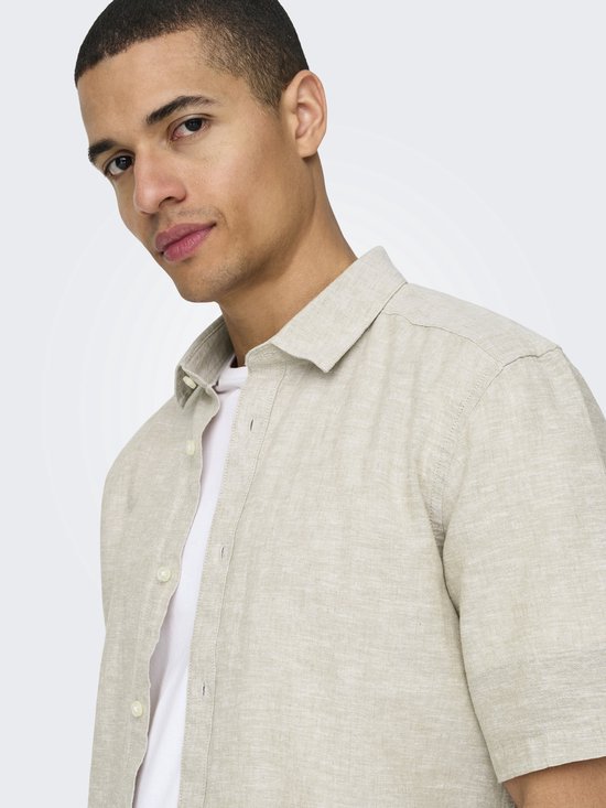 Close-up van een man die een beige linnen mix overhemd met korte mouwen draagt.