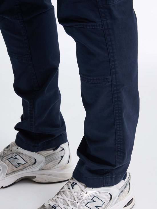 Donkerblauwe cargobroek met naden bij de knieën, gedragen met witte sneakers.
