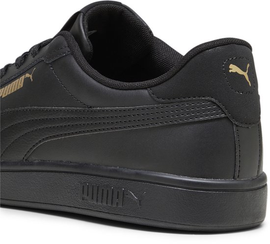 Close-up van de hiel van een zwarte sneaker met gouden Puma-logo's.