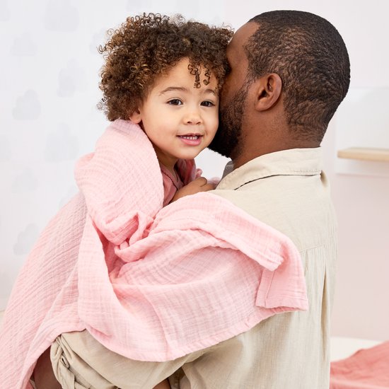 Man houdt een lachend kindje vast, gewikkeld in een zachtroze swaddle.