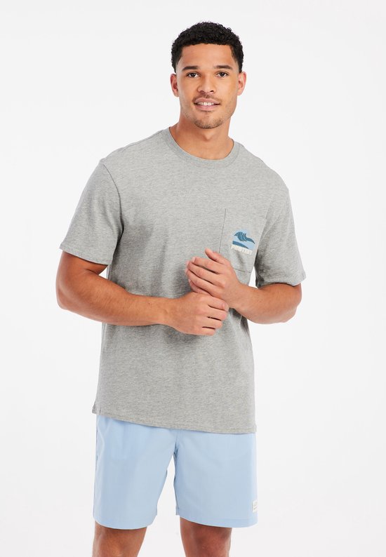 Model in een grijze t-shirt met borstzak met blauwe golfontwerp en lichtblauwe zwemshort.
