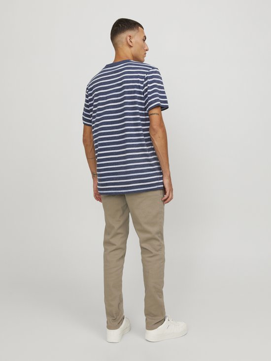 Model in een blauwgestreepte T-shirt en beige chino. De achterkant van het T-shirt is zichtbaar.