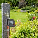 GARDENA besproeiingscomputer aangesloten op kraan, met slang, op stenen pilaar. Tuin.