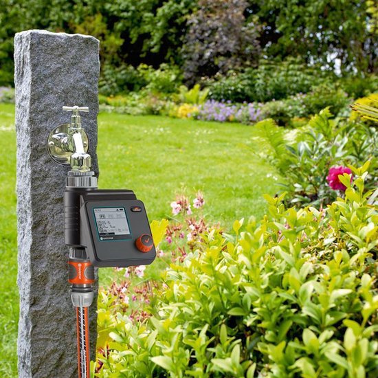 GARDENA besproeiingscomputer aangesloten op kraan, met slang, op stenen pilaar. Tuin.