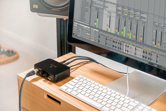 Zwarte RØDE AI-1 audio interface naast een computer met muzieksoftware, op een houten bureau.
