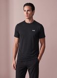 Vooraanzicht van een man in een zwart sportshirt met fijn gestreept patroon en SJS-logo, met hand in broekzak.