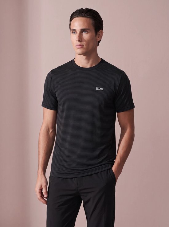 Vooraanzicht van een man in een zwart sportshirt met fijn gestreept patroon en SJS-logo, met hand in broekzak.