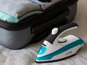 Wit en turquoise Lafe stoomstrijkijzer met zwarte handgreep, naast een koffer met kleding.