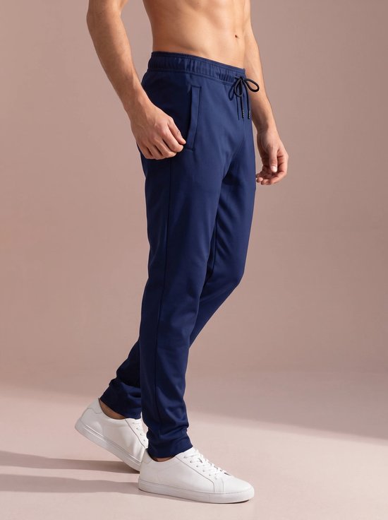 Marineblauwe joggingbroek met trekkoord en logo op linkerbeen, gedragen door een man met witte sneakers.