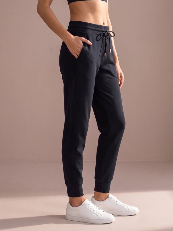 Donkerblauwe sportbroek met trekkoord, een rosé gouden veteroogje en zakken, gedragen door een model met witte sneakers.