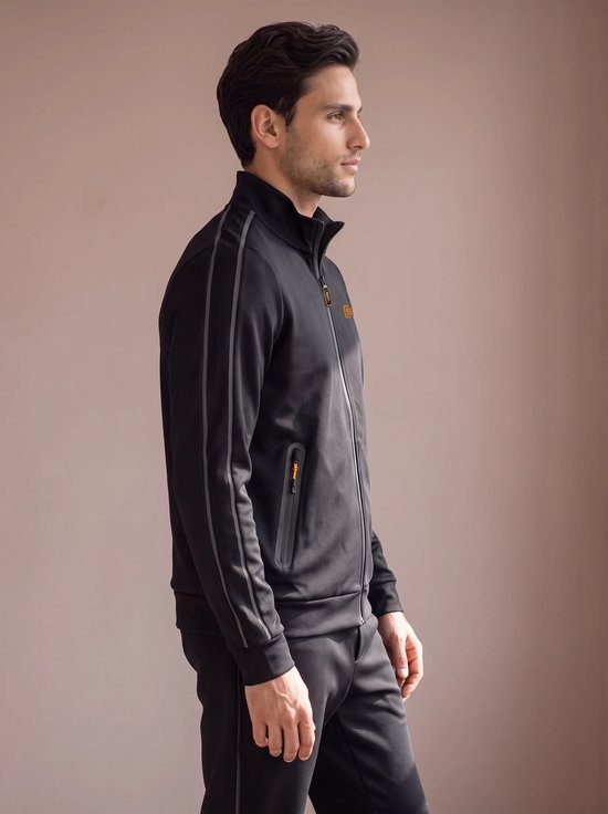 Man in zwart sportvest met grijze accentstrepen op de mouwen en oranje logo.