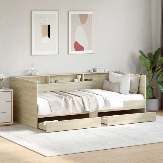 Gestyled licht eiken dagbed met beddengoed, kussens, open lades en een opbergrek aan de achterkant.