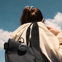 Zwarte, ronde Chipolo Bluetooth-tracker bevestigd aan een zwarte rugzak, gedragen door een persoon tegen een blauwe lucht.