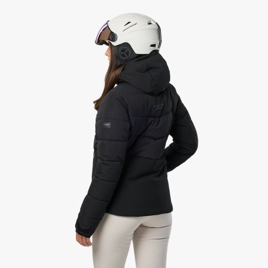 Zijaanzicht van een ski-jas voor dames in het zwart, gedragen met een witte skihelm.