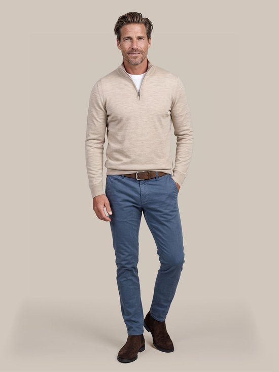 Model draagt een beige trui met rits, blauwe chino en bruine suède laarzen.