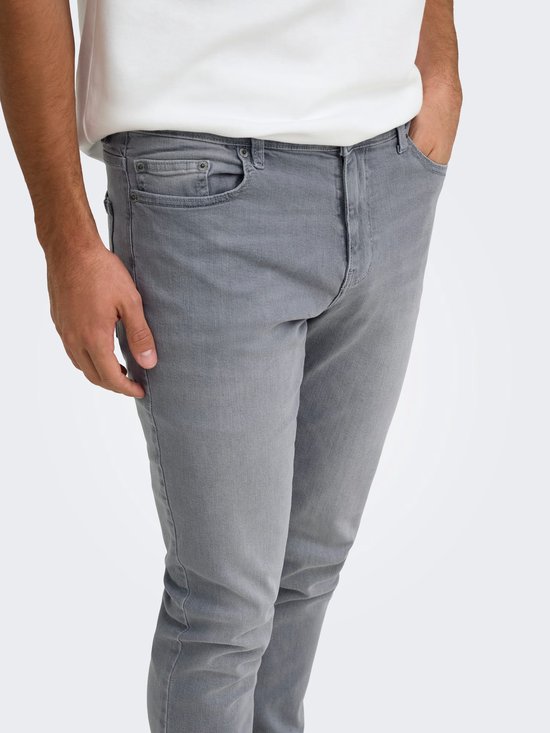 Close-up van de heup en zak van een grijze slim fit jeans op een model.