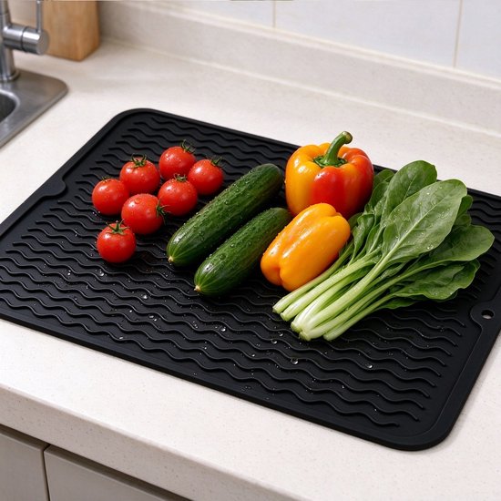 Zwarte siliconen mat op een aanrecht met verse groenten zoals tomaten, komkommers, paprika's en spinazie.