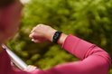 Close-up van persoon in roze sportshirt die naar een zwarte Fitbit Edge om de pols kijkt.