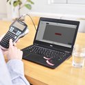 Persoon gebruikt een DYMO LabelManager 420P verbonden met een laptop om labels met de tekst PROMOTION te printen.