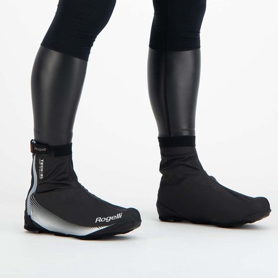 Zwarte Rogelli overschoenen met witte accenten, gedragen door een persoon met zwarte beenstukken.