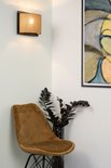 Een naturel bamboe wandlamp boven een bruin fluwelen stoel.