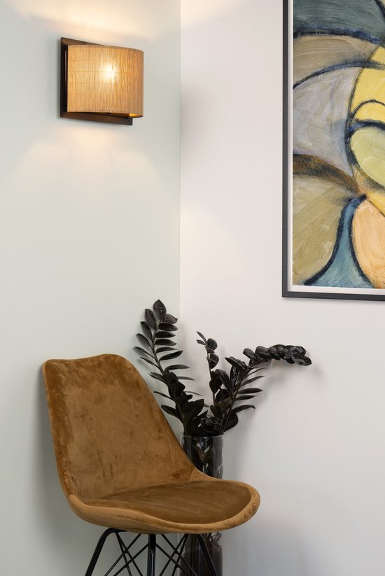 Een naturel bamboe wandlamp boven een bruin fluwelen stoel.