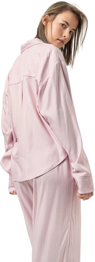 Zijaanzicht van model in roze gestreepte pyjamaset, kijkend over de schouder naar de camera.
