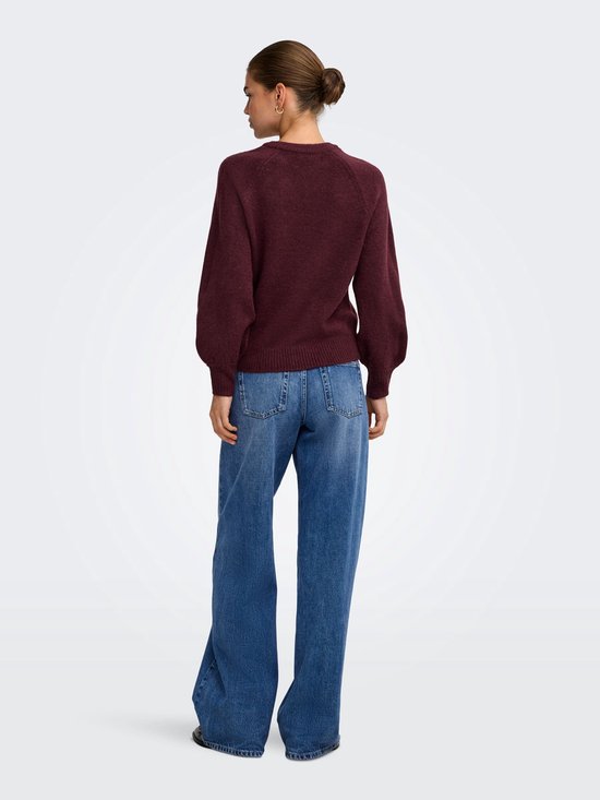 Vrouw met rug naar de camera, draagt een wijnrode gebreide trui met wijde jeans.