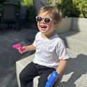 Een lachend jongetje met een roze Maesy kinderzonnebril, zittend met waterpistolen.