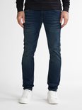 Man in donkerblauwe slim fit jeans met witte sneakers, voorkant benen.