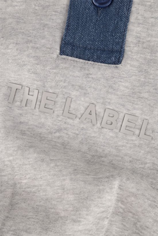 Grijze trui met blauwe denim knoopsluiting en de tekst 'THE LABEL' in reliëf.