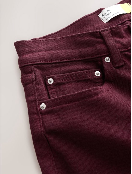 Close-up van de zakken en het 'SLIM MID RISE' label van de donkerrode stretchjeans.