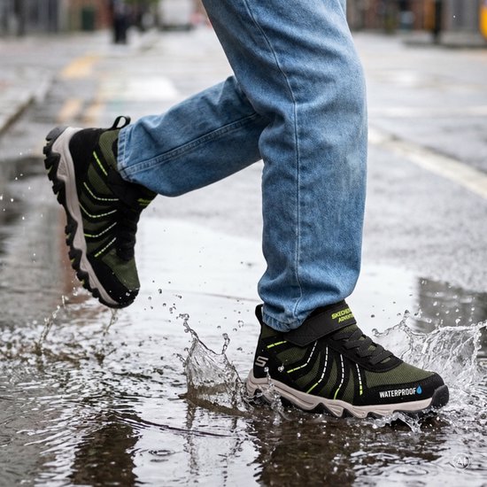 Olijfgroene en zwarte Skechers wandelschoenen met klittenband, 'Waterproof' tekst, terwijl ze in een plas spatten.