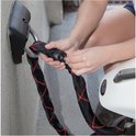 Iemand bevestigt een zwarte ketting met rood ruitpatroon aan een muuranker voor een scooter.
