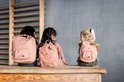 Drie kinderen op een bankje met verschillende formaten van de roze Mrs. Cat-rugzak op hun rug.