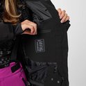 Vrouw opent een binnenzak van haar zwarte ski-jas, met technische informatie erop.
