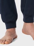 Close-up van de voeten van een man in een donkerblauwe pyjamabroek met elastische boorden onderaan.