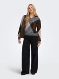 Model in een v-hals trui met argyle-patroon in grijs, bruin en beige, gedragen met zwarte wijde broek en een donkere tas.