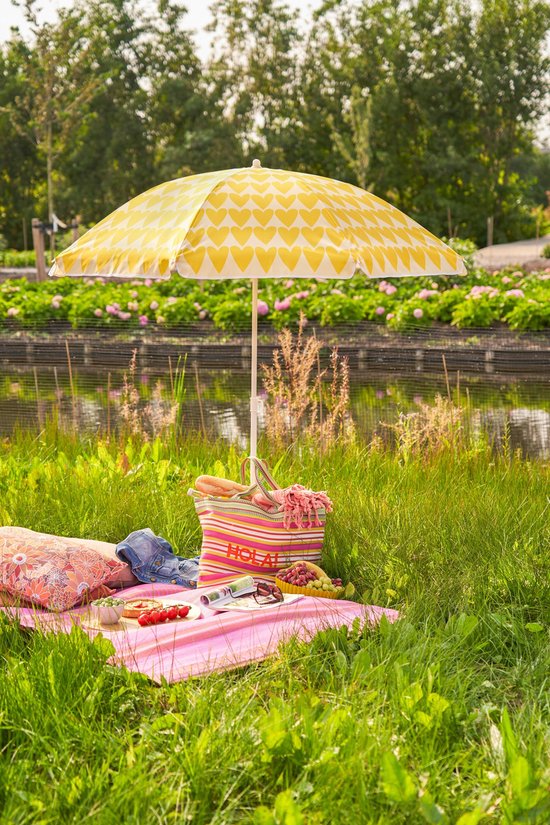 Gele parasol met wit hartjespatroon, staand in een picknickkleed met picknickspullen
