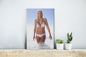 Canvas Schilderij Een blonde vrouw met een witte bikini loopt door het water - 20x30 cm - Wanddecoratie