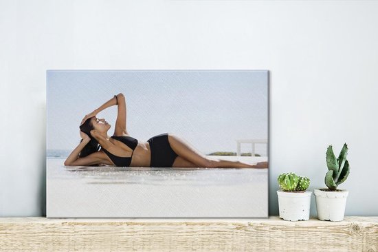 Canvas Schilderij Een vrouw in een zwarte bikini poseert op het strand - 30x20 cm - Wanddecoratie