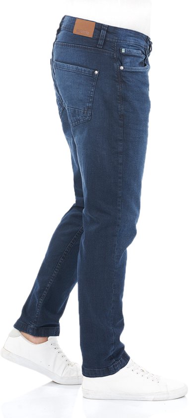 Man in een donkerblauwe regular/straight fit jeans, gezien vanaf de zijkant.