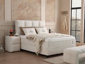 Een compleet opgemaakt wit boxspringbed met vierkant hoofdbord, nachtkastjes en een beige plaid.