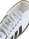 Witte sneaker met vetersluiting, zwarte Adidas strepen en suède neus.