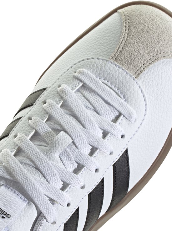 Witte sneaker met vetersluiting, zwarte Adidas strepen en suède neus.