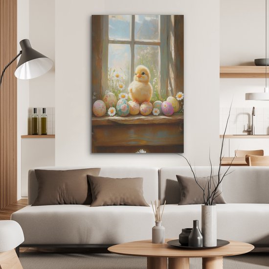 Schilderij van een kuiken en paaseieren op een vensterbank, hangend boven een bank in een woonkamer.