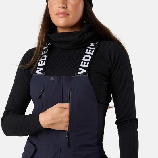 Detail van donkerblauwe skibroek met bretels met 'SWEDEMOUNT' tekst, model opent een rits.