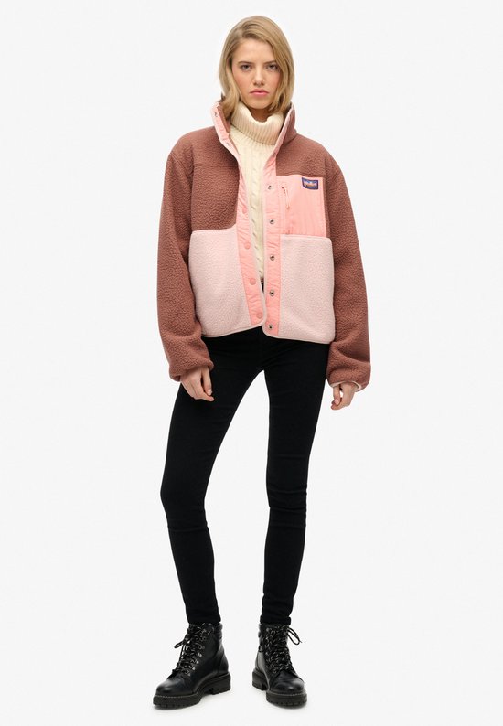 Model draagt bruine, roze en lichtroze fleece jas met zwarte broek.