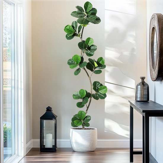 Grande plante artificielle verte avec de grandes feuilles dans un pot blanc dans un couloir près d'une fenêtre.