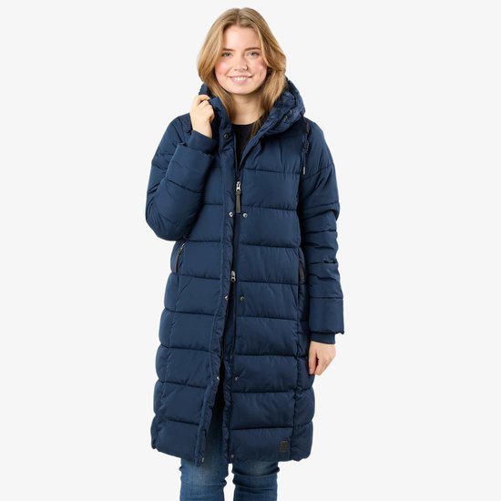 Vrouw voor een witte achtergrond, draagt een lange, donkerblauwe, gewatteerde winterjas.